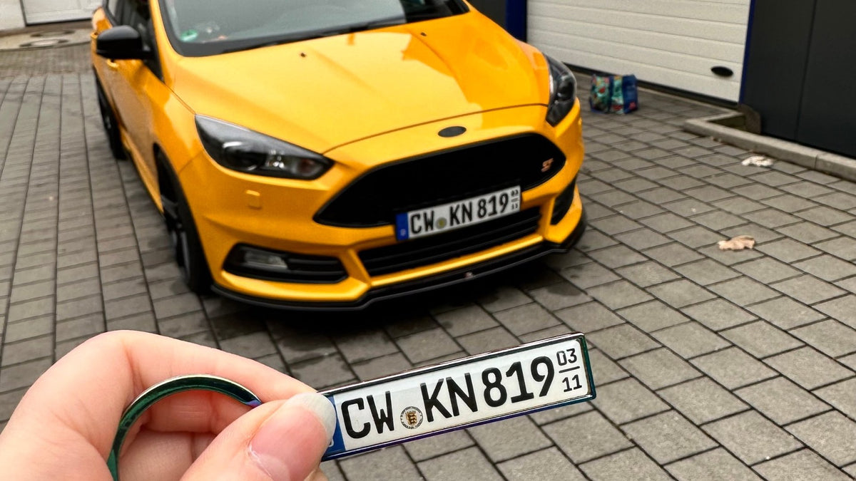 Mini-Kennzeichen als Schlüsselanhänger vor dem Auto mit dem gleichen Kennzeichen